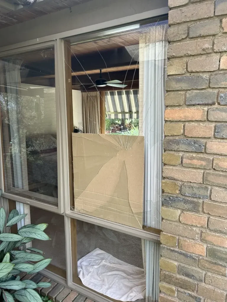 Damaged glass in a window beside a brick wall before replacement