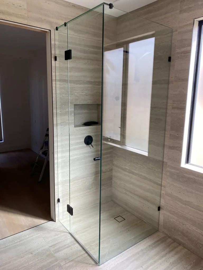 Clear frameless corner shower enclosure with black hinges and handle