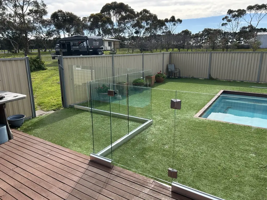 Glass pool fence beside a swimming pool and lawn